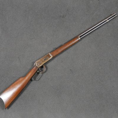 un fusil avec une crosse en bois posée sur une surface grise