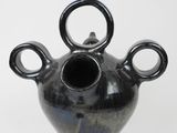 a black vase with three handles on it on a white surface
