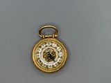 une image représentant une montre de poche en or posée sur une surface grise