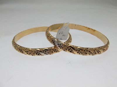 two gold bang bracelets with engraved designs on them on a white surface