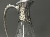 a clear glass pitcher with a silver handle on a table