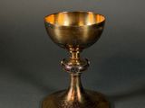 an antique brass chalicet on a stand against a gray background