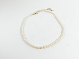 un collier de perles blanches muni d'un fermoir en or, posé sur un fond blanc