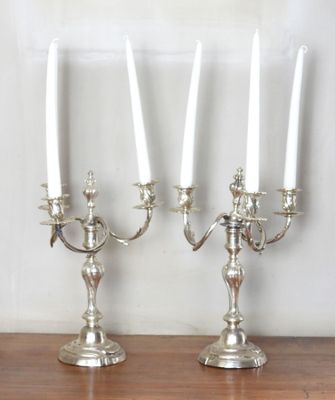 two silver candelabs with white candles on a wooden table