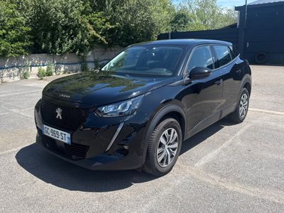 La voiture noire est garée sur le parking, près des arbres.