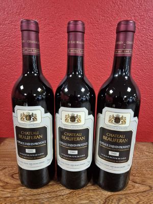 Trois bouteilles de vin du Château Realfron sont posées sur une table en bois.