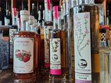 bottles of liquor lined up on a wooden table in front of a shelf full of bottles