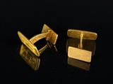 two gold cufflinks on a black surface with a black background