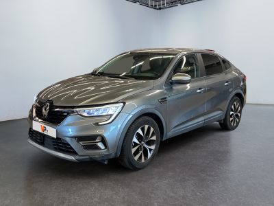 La voiture grise est garée dans le showroom, devant un mur blanc.