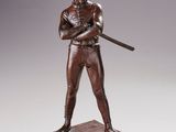 statue en bronze représentant un joueur de baseball tenant une batte, posée sur un socle en bois
