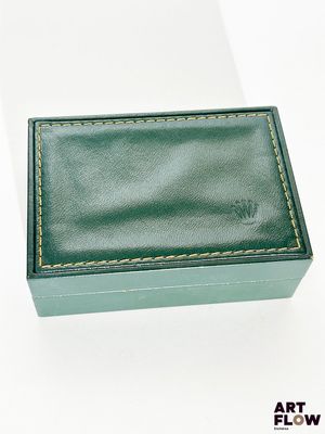 boîte à bijoux en cuir vert posée sur une surface blanche, sur fond blanc