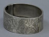 silver bracelet with a design of leaves and flowers on it