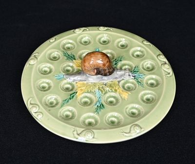 une assiette verte sur laquelle est représenté un escargot, posée sur une surface noire