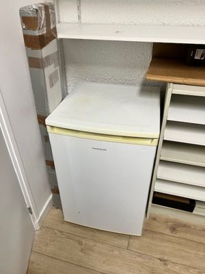 un petit réfrigérateur blanc dans le coin d'une pièce