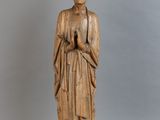 une vieille statue en bois représentant une femme, les mains dans les poches