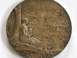 une médaille de bronze représentant un homme assis sur un banc