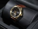La montre est présentée dans un coffret noir, avec un bracelet en cuir marron.