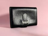 a black leather wallet with a metal clasp on a pink background