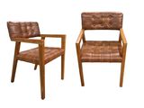 deux chaises en cuir marron assises l'une à côté de l'autre sur une surface blanche