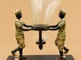 statue représentant deux hommes tenant un grand vase en verre posé sur un socle noir