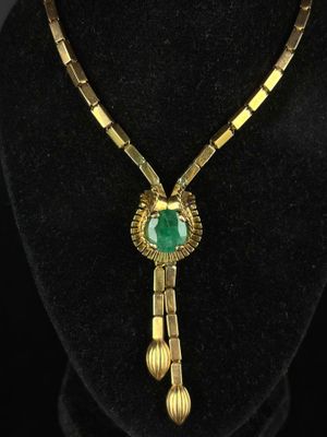a gold necklace with a green stone pendant on a black mannequin