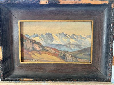 une peinture à l'huile représentant un paysage de montagne, encadrée dans un cadre en bois et posée sur une table