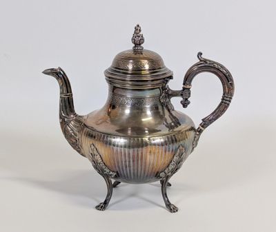 une théière ancienne en argent, avec une anse en forme d'oiseau, posée sur un socle