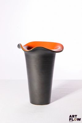 a black vase with an orange handle sitting on a white surface