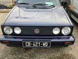 une Volkswagen Golf bleue garée sur un parking à côté d'une camionnette