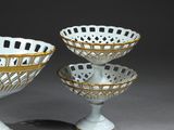 pair of white and gold glass bowls on pedestals on a gray surface
