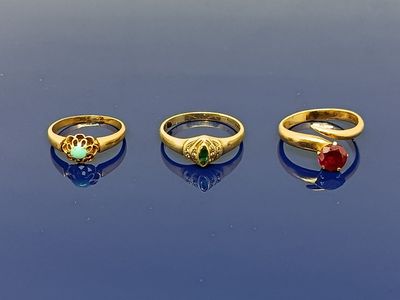 trois bagues en or ornées de pierres de différentes couleurs reposent sur un fond bleu