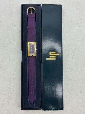 une montre violette dans un coffret noir, à côté d'un coffret vert