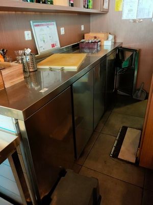 une petite cuisine équipée d'un plan de travail en inox et d'un réfrigérateur