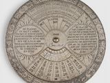 a silver plate with a sundial on it on a white surface