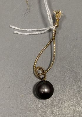 collier composé d'une perle noire et d'une chaîne en or sur un fond gris