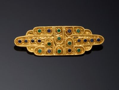 un gros plan d'une broche en or sertie de pierres vertes et bleues