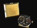 a gold watch and a gold box on a black surface