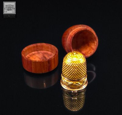 a close up of a thimble and a wooden box on a black surface