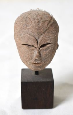 une sculpture en pierre représentant un visage, posée sur un socle en bois