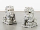 une paire de statues en marbre blanc représentant des « foo foo foo » posées sur un sol gris