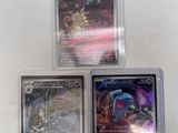 three different pokemon cards in plastic cases on a white surface