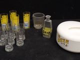 Des bouteilles et des verres sont alignés sur une table, à côté d'un récipient blanc.