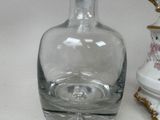 a clear glass bottle with a gold handle next to a white vase