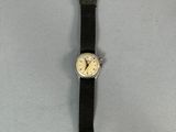 La montre repose sur une surface blanche et est dotée d'un bracelet noir.