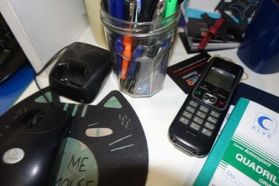 une tasse remplie de stylos, un téléphone portable et une souris posés sur un bureau