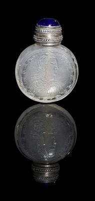 flacon à priser en verre argenté et bleu posé sur une surface réfléchissante