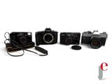 four cameras are lined up on a white surface with a camera strap