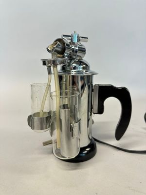 a silver coffee maker with a glass in front of it