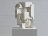 une sculpture blanche posée sur un socle devant un mur de briques