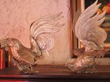 two statues of roosters on a table in front of a painting